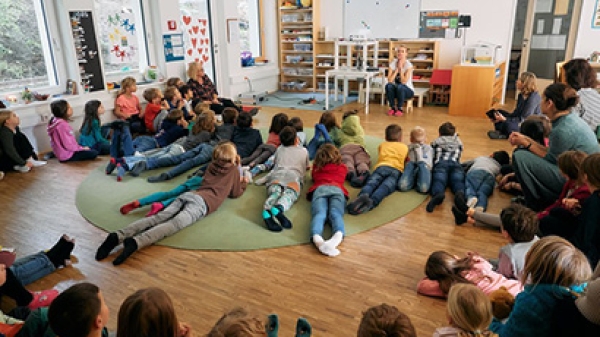 Children are sitting on the floor in a classroom in front of a teacher