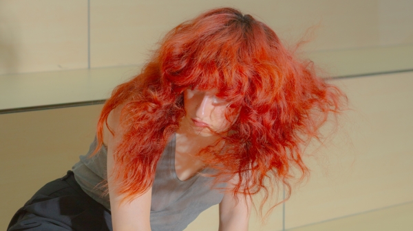 A person with long red hair kneeling on a wooden platform. 