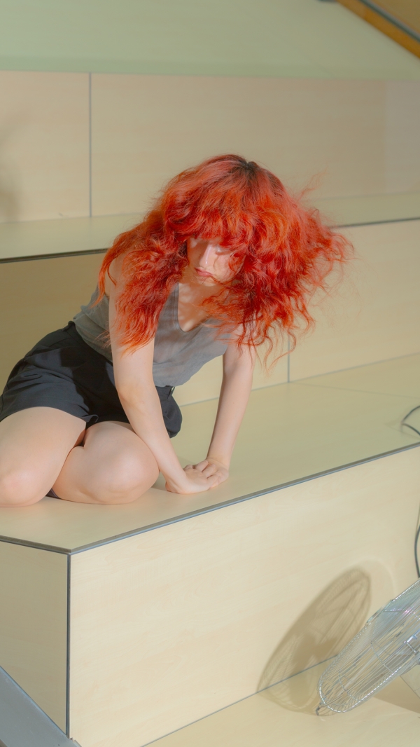 A person with long red hair kneeling on a wooden platform. 