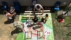 Kinder und Erwachsene arbeiten an einem Holzobjekt im Freien, , Summer
                                          School im Rahmen des Projekts Lunik CoLab
