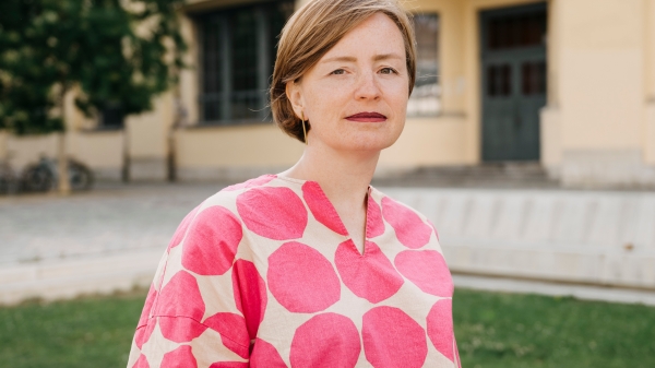 Porträt in Farbe von Ulrike Kuch vor grüner Wiese und einem Gebäude im Hintergrund